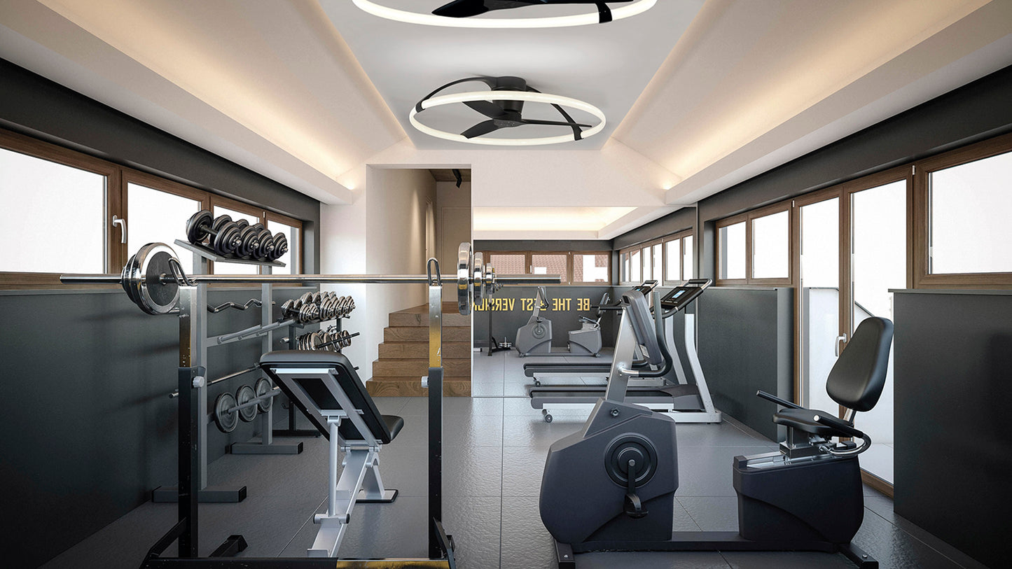 A brightly lit gym with modern equipment, including weight racks, a squat rack, exercise bikes, and treadmills. Large windows line the walls, allowing natural light to pour in. The phrase "Be the best version of you" is visible on the wall in the background, illuminated by Nepal Black Ceiling Fans with light from Ceiling Fans UK.