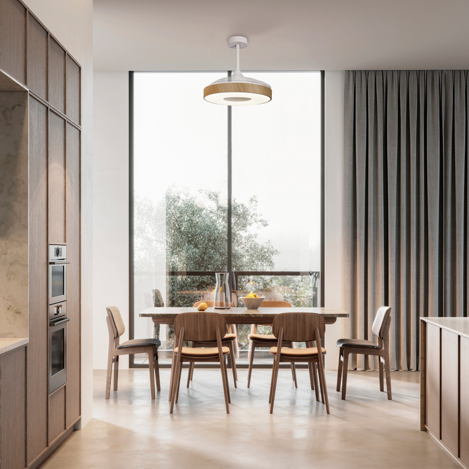 A modern dining area with a wooden table and six chairs set against large, floor-to-ceiling windows. The table holds a carafe, glassware, and a bowl of fruit. The room features light wooden cabinetry, a neutral color palette with tall curtains on the right, and an elegant Ceiling Fans UK Coin White/Wood Ceiling Fan with light 60W LED Dimmable Ceiling Light With Built-In 30W DC Reversible Fan, Remote & APP Control, backed by a 5-year warranty.