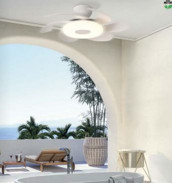 A bright, modern interior features the Flower White/Wood Ceiling Fan with Light by Ceiling Fans UK, boasting 50cm curved blades and a dimmable 24W LED light. Below, a luxurious bathtub faces an outdoor archway that frames a scenic view of trees, a distant body of water, and lounge furniture on a patio. The space is airy and serene.