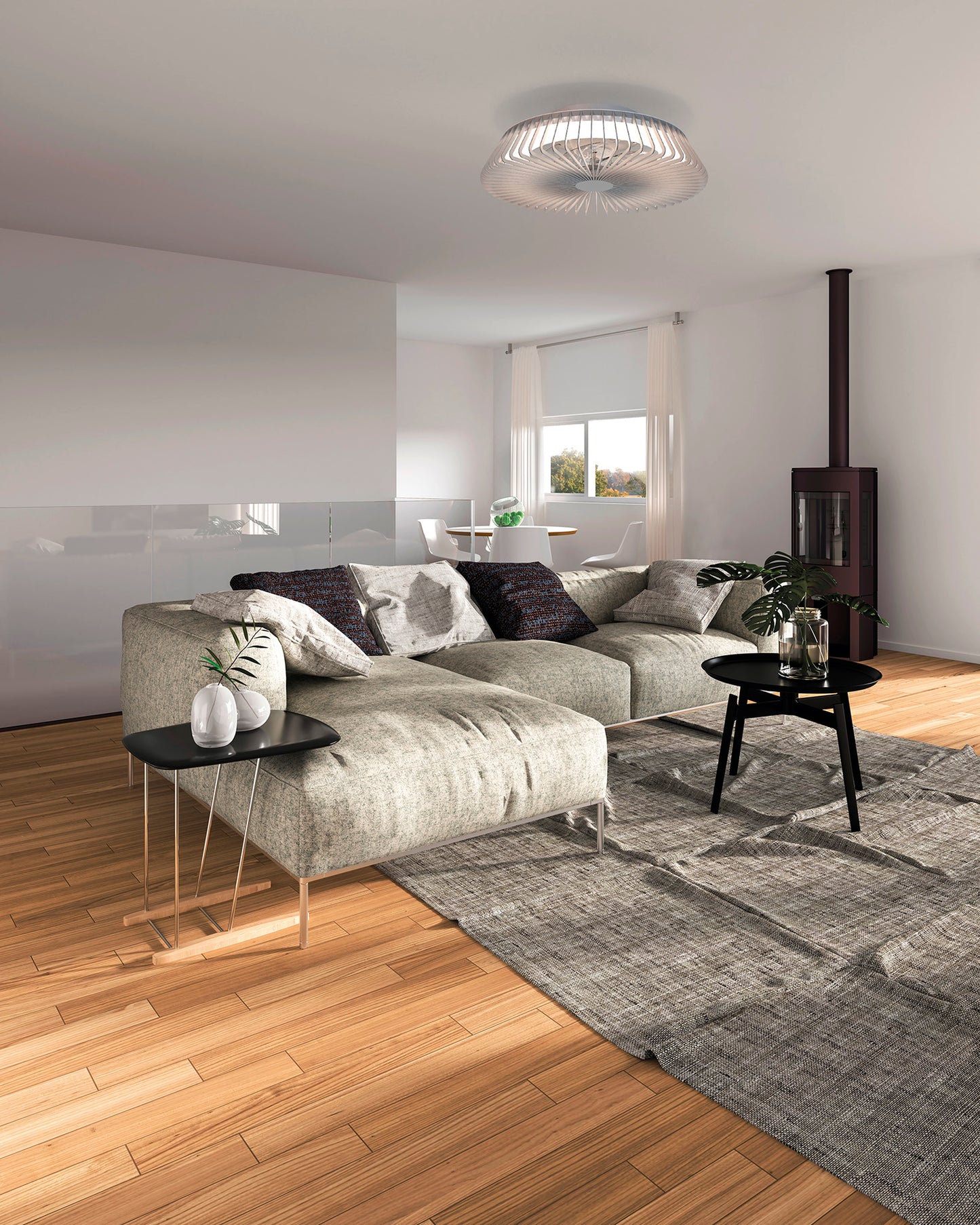 A modern living room features a light gray sofa, black side tables, and a gray rug on hardwood flooring. A Ceiling Fans UK Himalaya Silver Ceiling Fan with Light enhances the elegance above, while the wood-burning stove in the corner provides warmth. Natural light streams through white curtains near the window, accentuating the cozy ambiance.