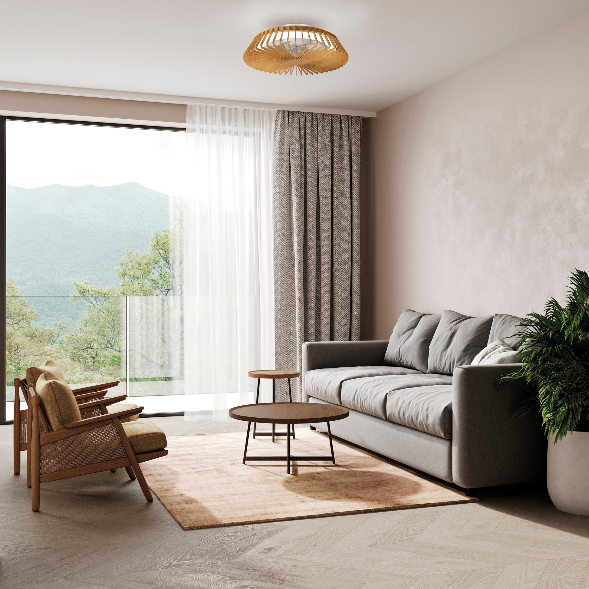 A modern living room features a gray sofa, two wooden chairs with beige cushions, a round coffee table, and a matching side table on a light brown rug. A large window with sheer curtains overlooks a scenic mountain view. A potted plant and the Himalaya Mini Wood Ceiling Fan with Light by Ceiling Fans UK complete the space, providing adjustable lighting from 2700-5000K.