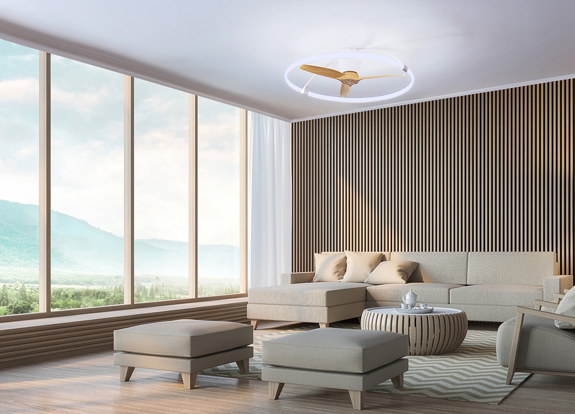 A modern living room with large floor-to-ceiling windows offering a scenic view of mountains. The room features a neutral-toned sectional sofa, round coffee table, two ottomans, and a wood-paneled accent wall. Hanging above is the Ceiling Fans UK Nepal White/Beech Ceiling Fan with light 105cm 75W LED Dimmable Light With Built-In 35W DC Reversible Fan, complete with remote control as well as APP & Alexa/Google Voice Control and boasting an impressive 7200lm.