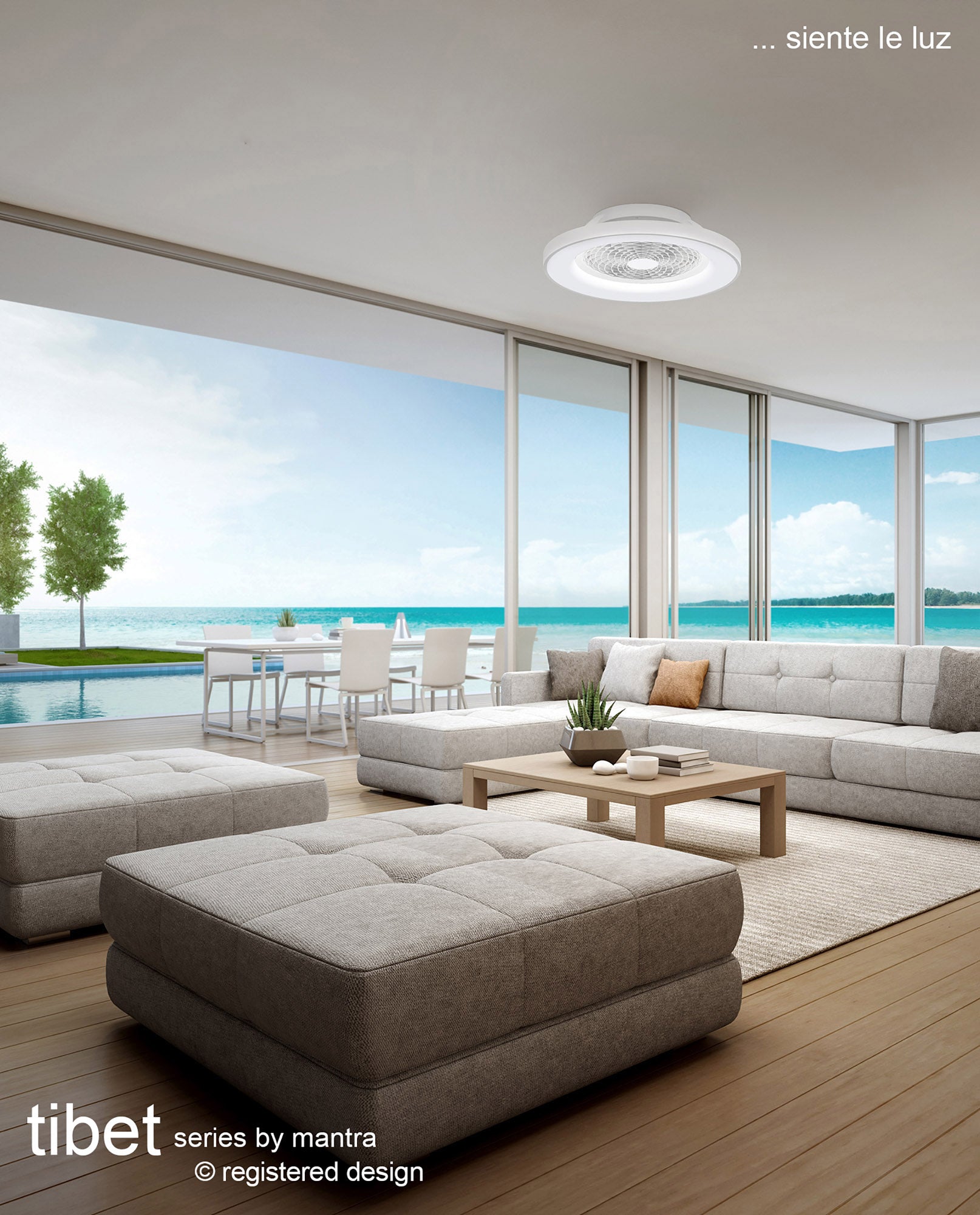 A modern living room with large glass doors overlooks a pool and ocean view. The room features a light gray sectional sofa, matching ottomans, and a wooden coffee table. Highlighted in the space is the Tibet White Ceiling Fan with light - a 65cm dimmable 70W LED fixture that includes a 35W DC reversible fan. This stylish piece from Ceiling Fans UK comes with remote control, APP & Alexa/Google Voice compatibility, and is backed by a 5-year warranty. Text: "Tibet series by mantra" and "siente le luz".